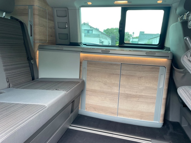 Blick durch die Schiebetür auf das umgebaute Bett und die Küchenschränke des VW California Coast