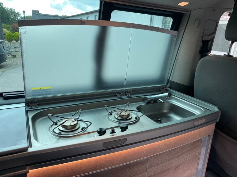 Küchenzeile des VW California Coast mit zwei Gaskochern, Spüle und aufgeklapptem Spritzschutz