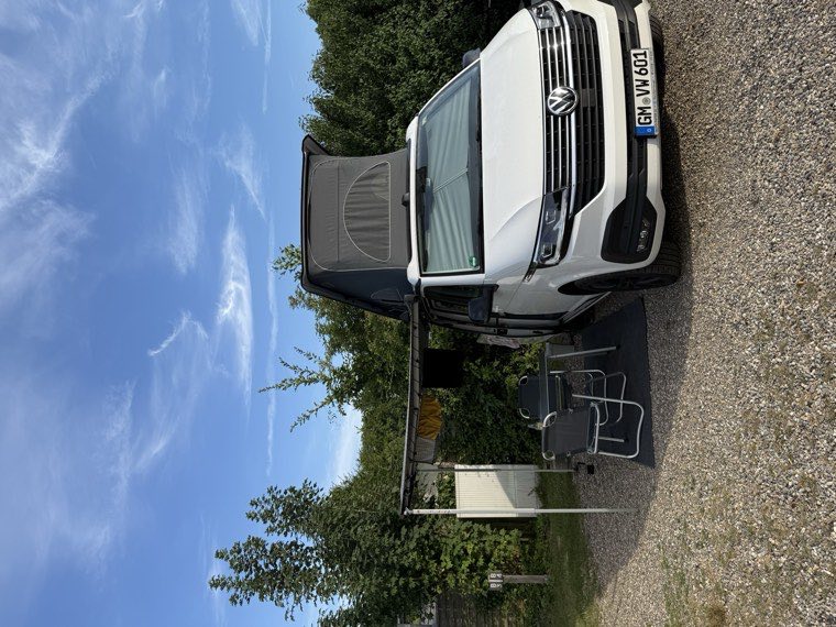 VW California Coast auf einem Stellplatz, Markise ausgefahren, Tisch und Stühle aufgebaut