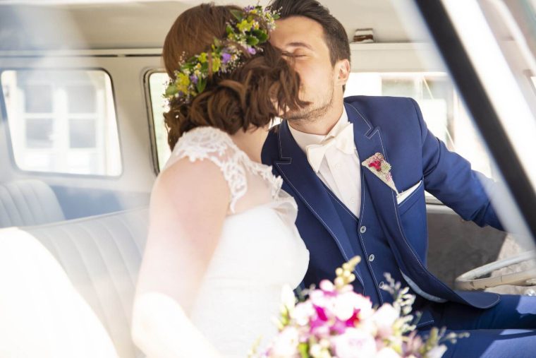 Braut und Bräutigam sitzen lachend im Fond des Bulli, die Braut mit Blumenkranz im Haar