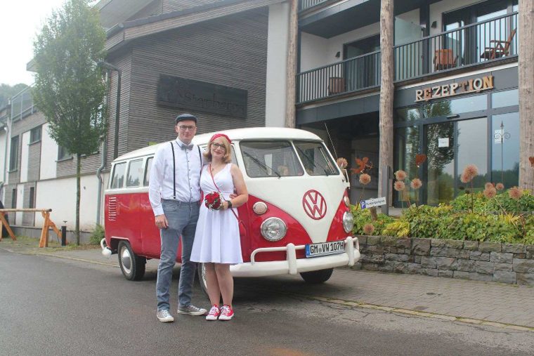 Ein Paar im Vintage-Look posiert vor dem Bulli am Eingang eines Hotels