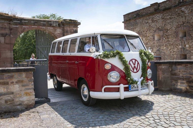 Rot-weißer Bulli mit Blumenschmuck vor einer alten Burgmauer
