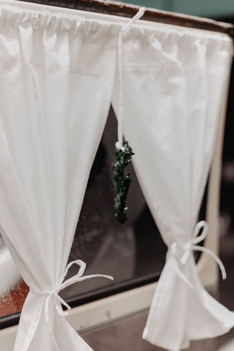 Weiße Vorhänge mit Schleife im Bulli-Fenster, dezent für die Hochzeit drapiert
