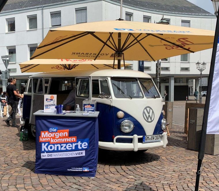 Blauer Bulli mit Volksbanken-Promotionstand und Sonnenschirmen auf einem Marktplatz