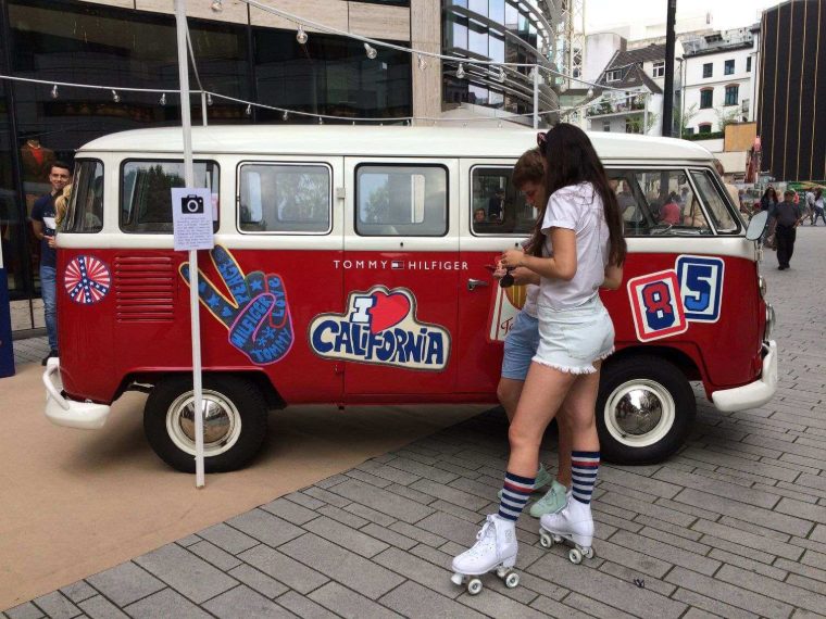 Tommy-Hilfiger-Bulli mit „I Love California“-Motiv, davor zwei Personen auf Rollschuhen
