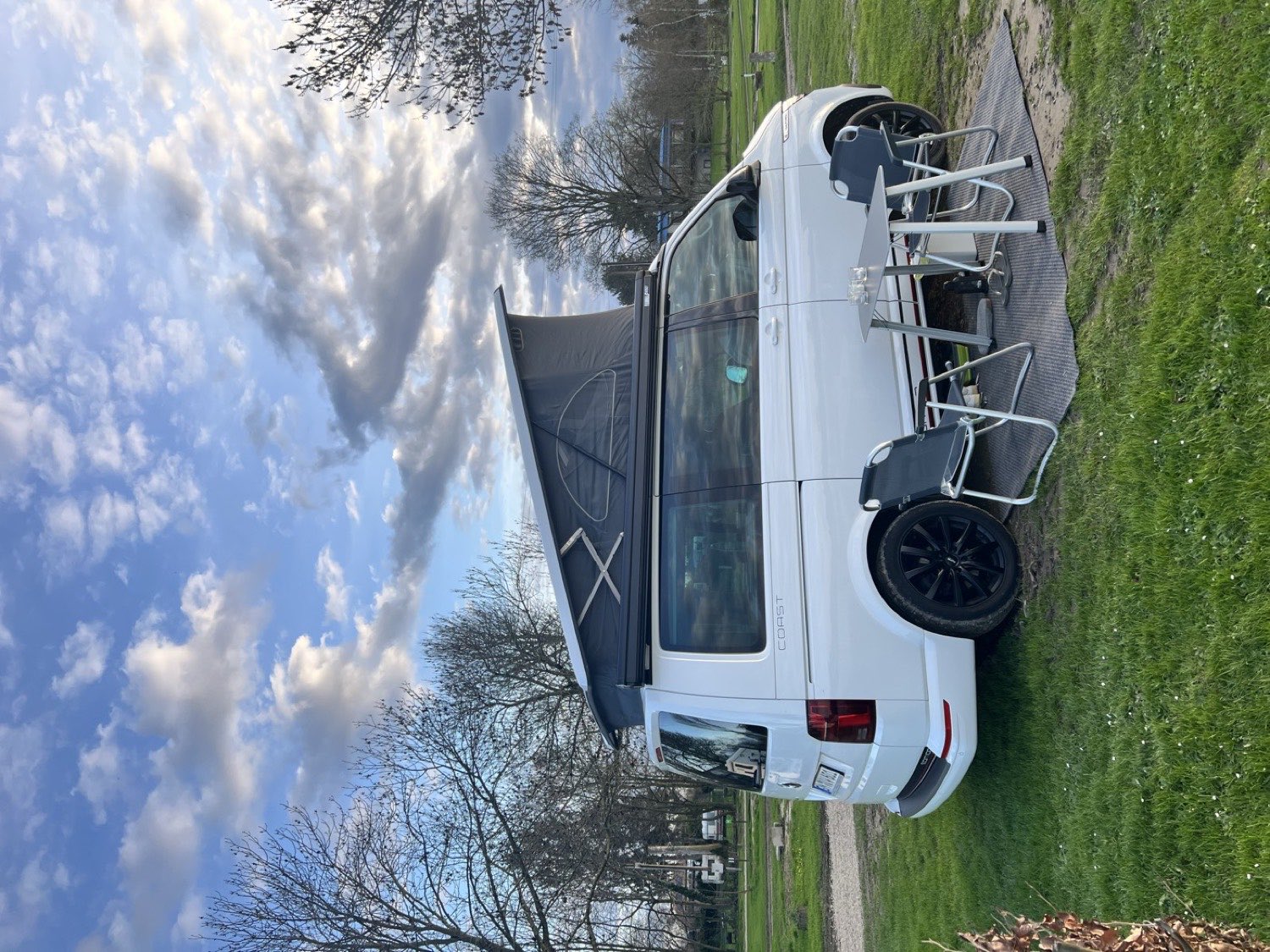 VW California Coast mit ausgefahrener Markise, Tisch und St&uuml;hlen auf einer Wiese