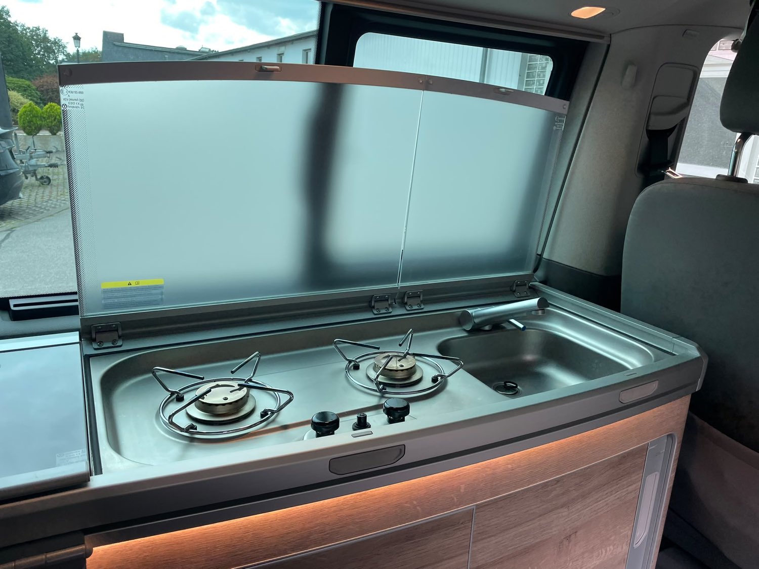 Küchenzeile des VW California Coast mit zwei Gaskochern, Spüle und aufgeklapptem Spritzschutz