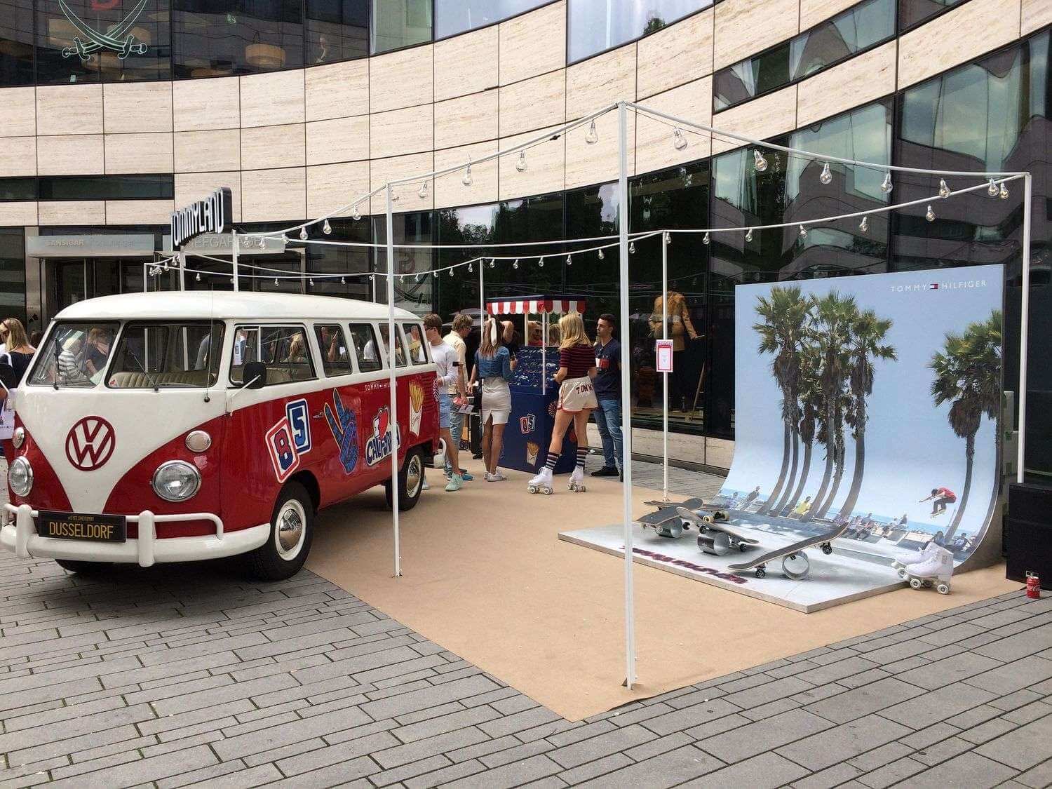 Rot-weißer VW T1 Bulli mit Markenbeklebung als Blickfang eines Ausstellungsstands vor einem Einkaufszentrum, daneben eine Displaywand