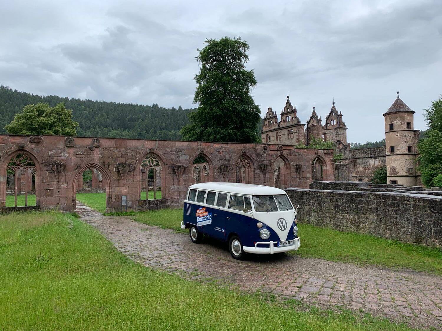Blau-weißer VW T1 Bulli mit Markenbeklebung auf dem Weg zum Einsatzort, geparkt vor einer historischen Klosterruine