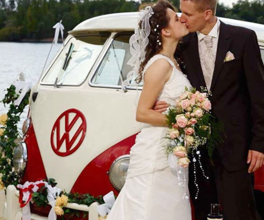 Ein Brautpaar küsst sich vor dem geschmückten VW Hochzeitsbulli während der Fotosession