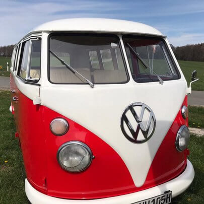 Frontaufnahme eine Oldtimer Bulli mit Safari-fenstern von 1964 und verchromten VW Emblem rot-weiss lackiert