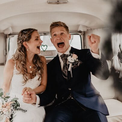 Hochzeitspaar im Hochzeitsfahrzeug Volkswagen Bulli auf original Bänken sitzend