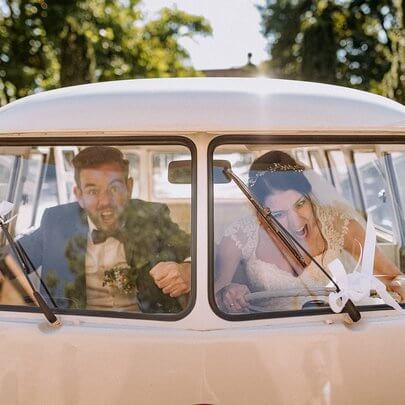 VW Bulli Hochzeitsauto mit Brautpaar in der Front hinter den schönen Safari-Fenstern