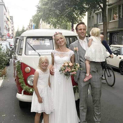 Dekorierter VW Bulli rot-weiss lackiert mit frisch vermähltem Brautpaar in der Stadt