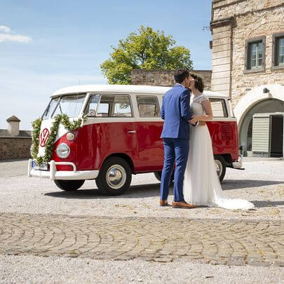 Brautpaar küsst sich vor dem dekoriertem  VW Bulli T1 auf dem Schlosshof