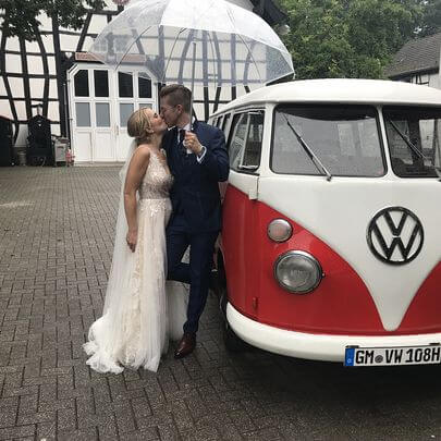 Brautpaar küsst sich vor dem VW Bulli T1 rot-weiss lackiert im Regen