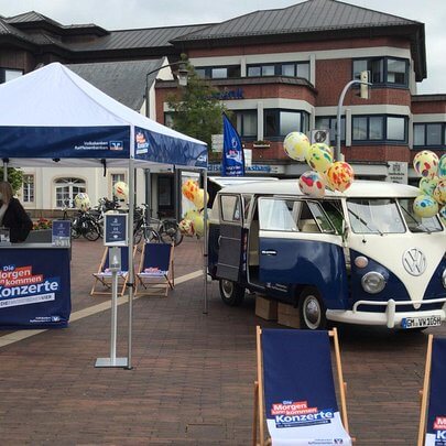 VW Bulli Oldtimer als Promotinfahrzeug bei einem Werbestand in einer Stadt 